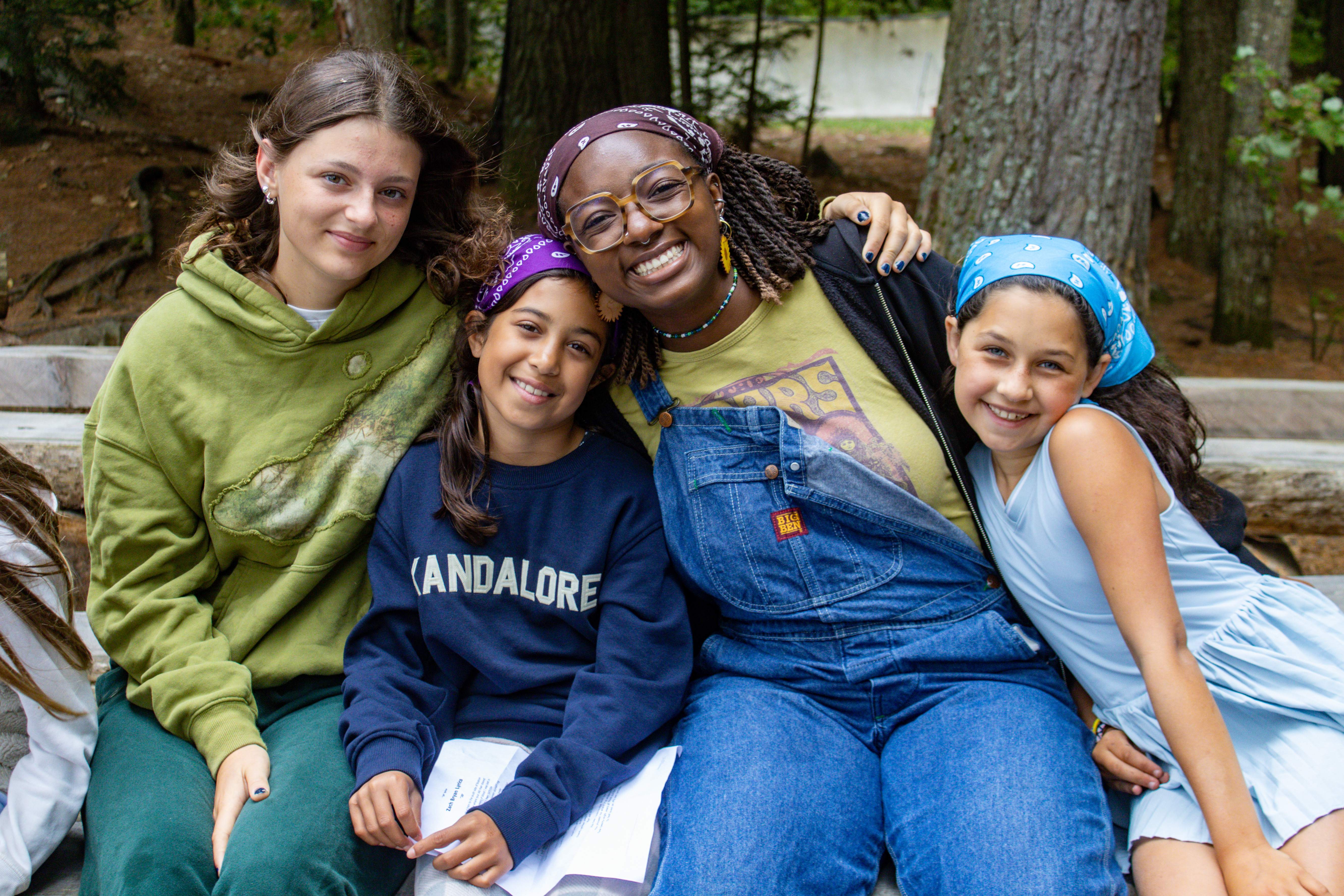 A camp counsellor sitting with three campers, smiling together in the forest